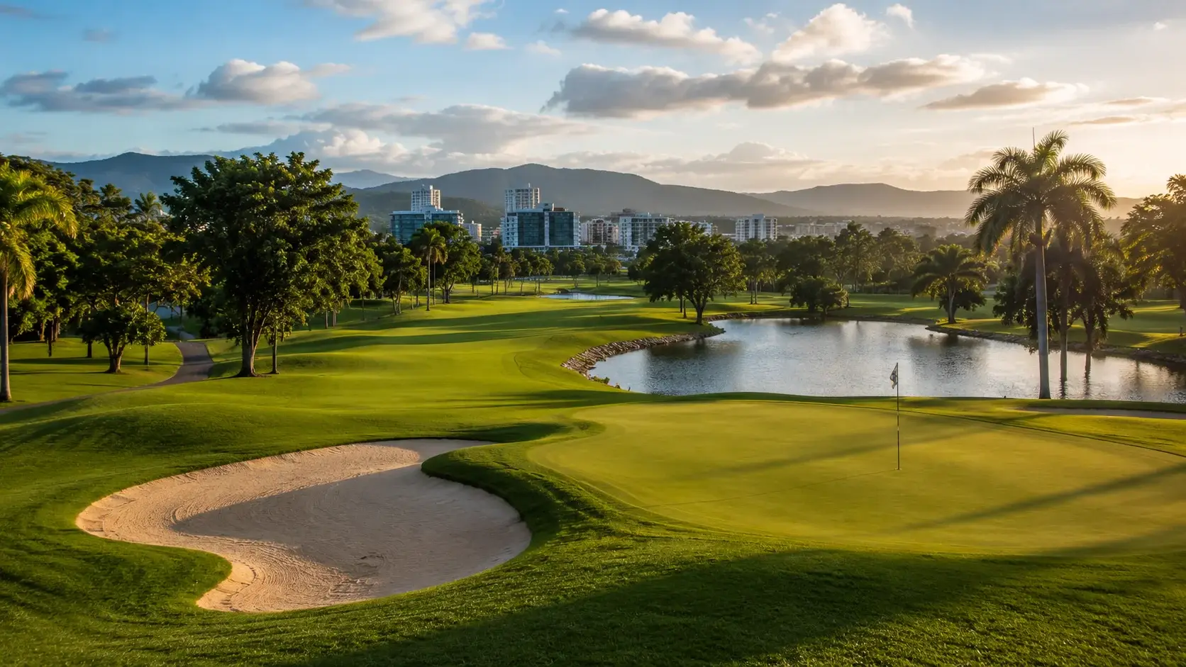Scenic golf course in Guaynabo, Puerto Rico, featuring manicured fairways, lakes, palm trees, and panoramic mountain views at sunset.