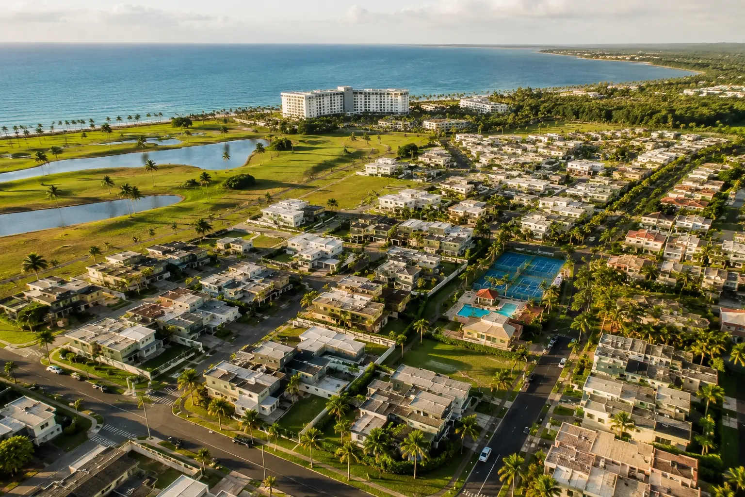 Aerial view of Sabanera Dorado in Dorado, Puerto Rico, featuring luxury homes, landscaped streets, lakes, sports facilities, and the nearby Caribbean coastline.