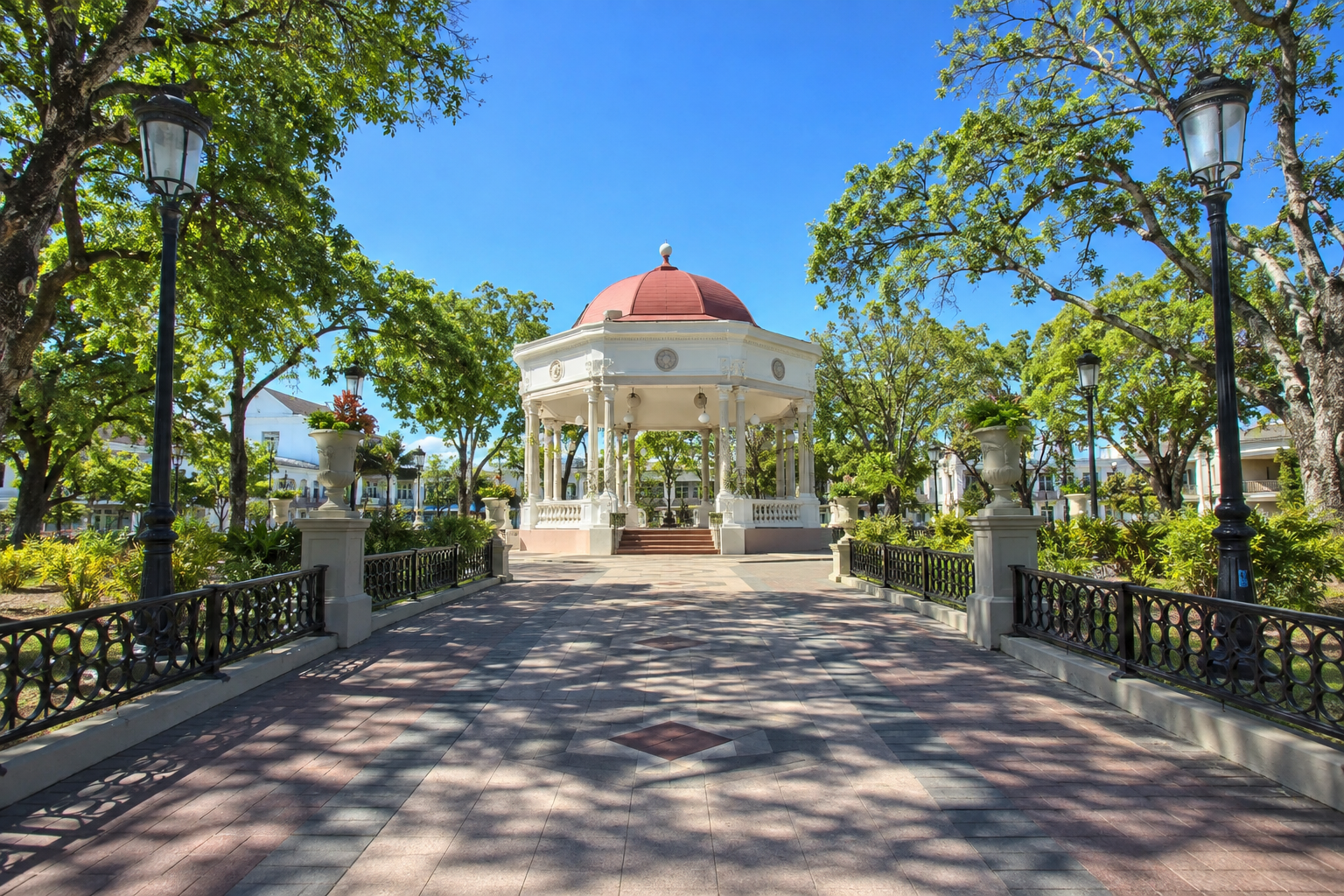 Tree-lined walkway leading to a red-roofed gazebo in Plaza Las Delicias, Ponce.