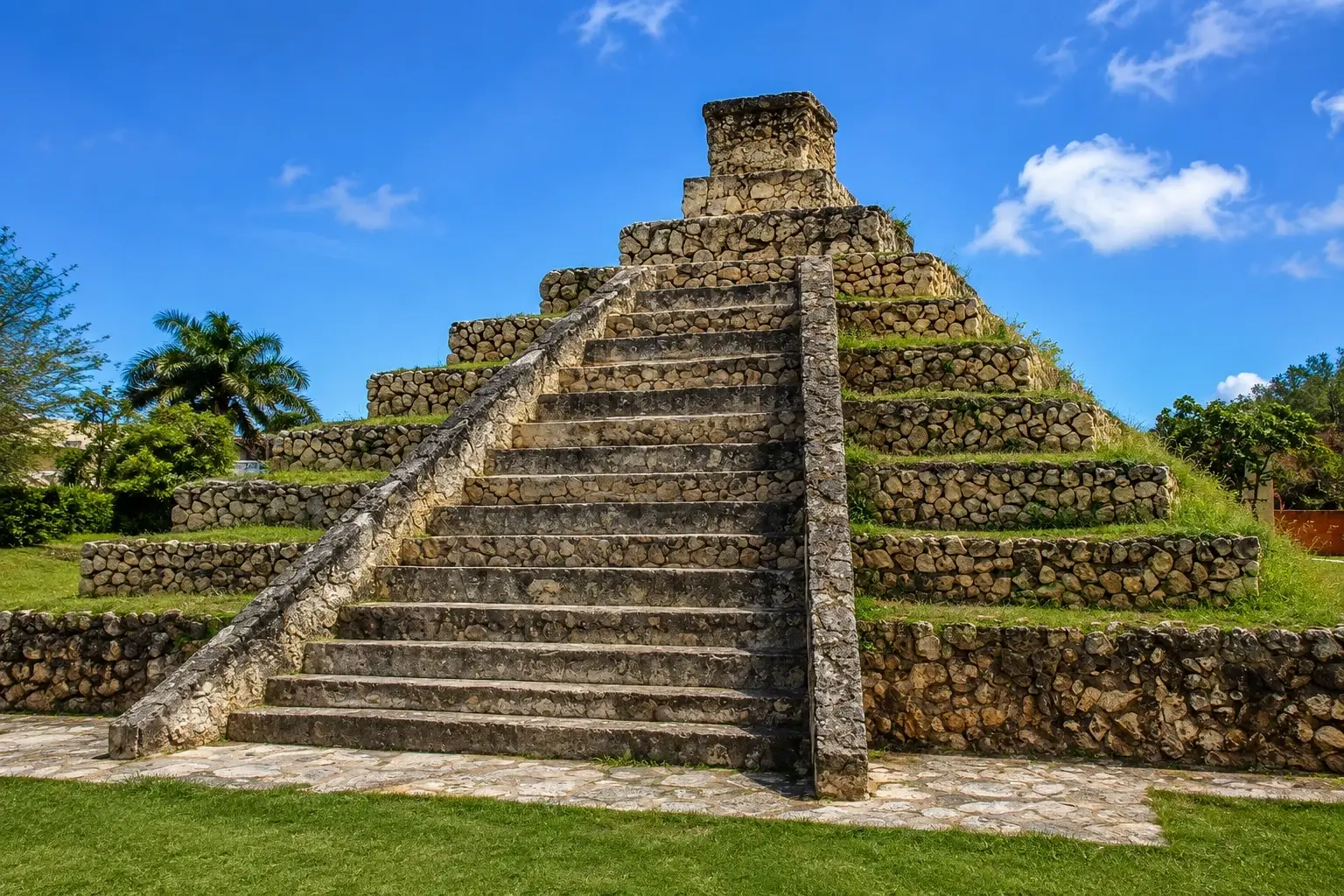 Stepped stone Aguada Pyramid in Aguada, Puerto Rico, with a central staircase, tropical greenery, and a bright blue Caribbean sky.