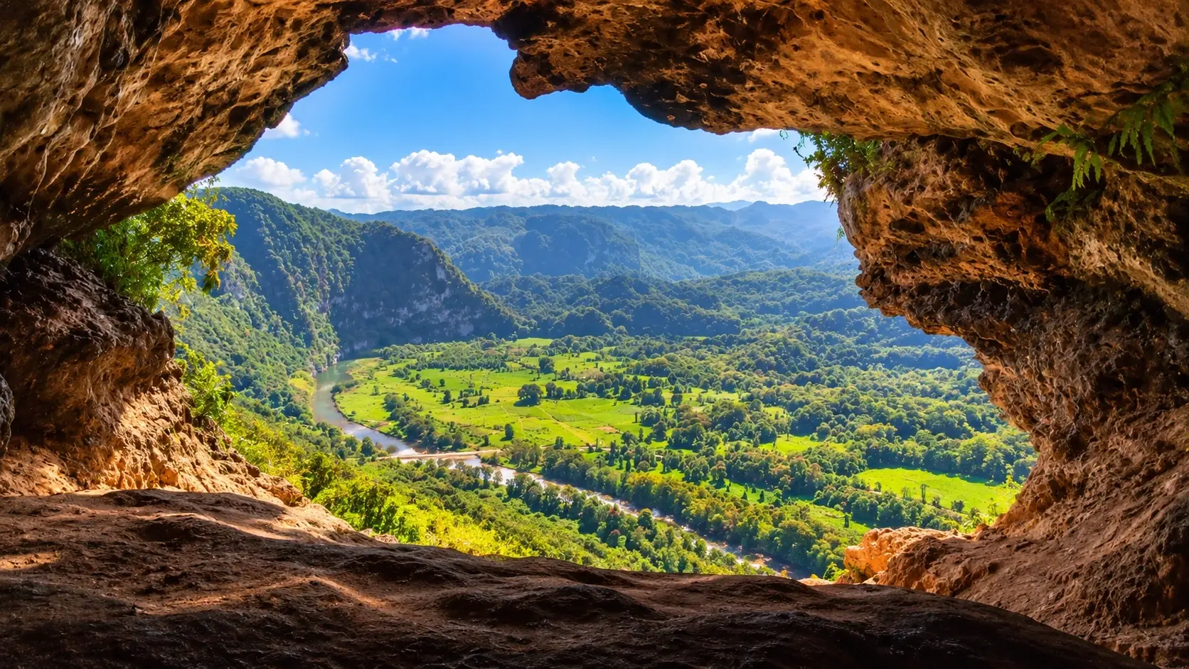 Scenic mountain valley in Aibonito, Puerto Rico, viewed through a rocky cave opening surrounded by lush tropical nature.