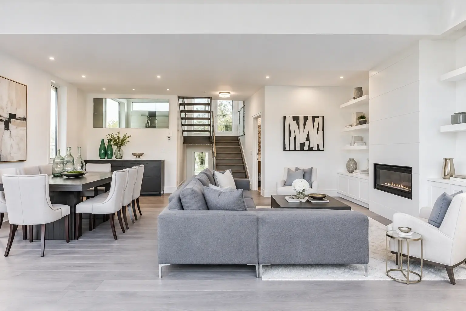 apartment-home-usa Open-plan interior with a gray sofa, dining area, staircase and fireplace.
