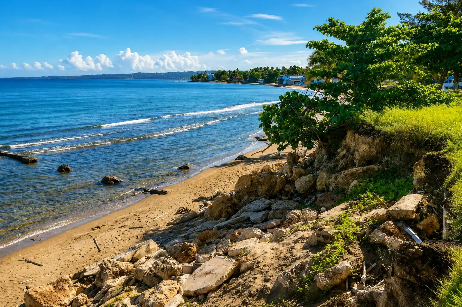 Scenic coastal view of Aguada, Puerto Rico, with a sandy beach, calm blue ocean, rocky shoreline, tropical greenery, and seaside scenery.
