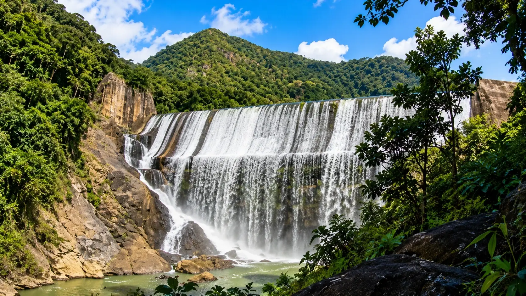 Scenic representation of Cerro La Tiza in Aguas Buenas, Puerto Rico, with a broad waterfall, lush tropical forest, rocky cliffs, green mountains, and a natural pool.