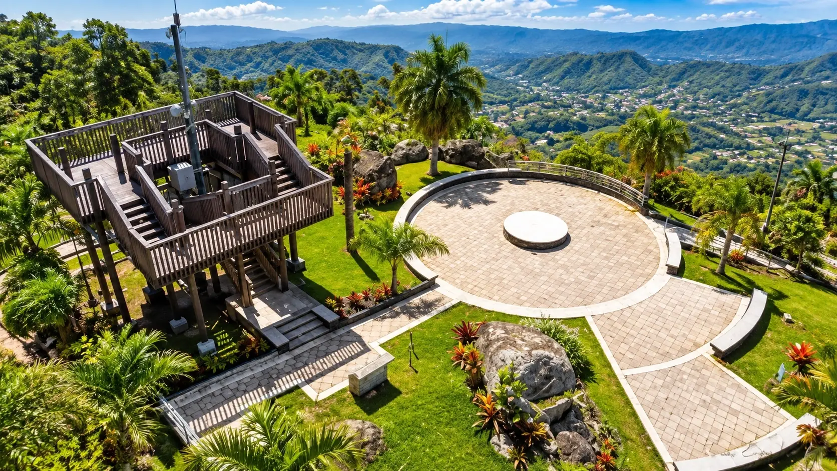 Aerial view of Mirador Piedra Degetau in Aibonito, Puerto Rico, with an observation structure, landscaped plaza, tropical gardens, and panoramic mountain scenery.