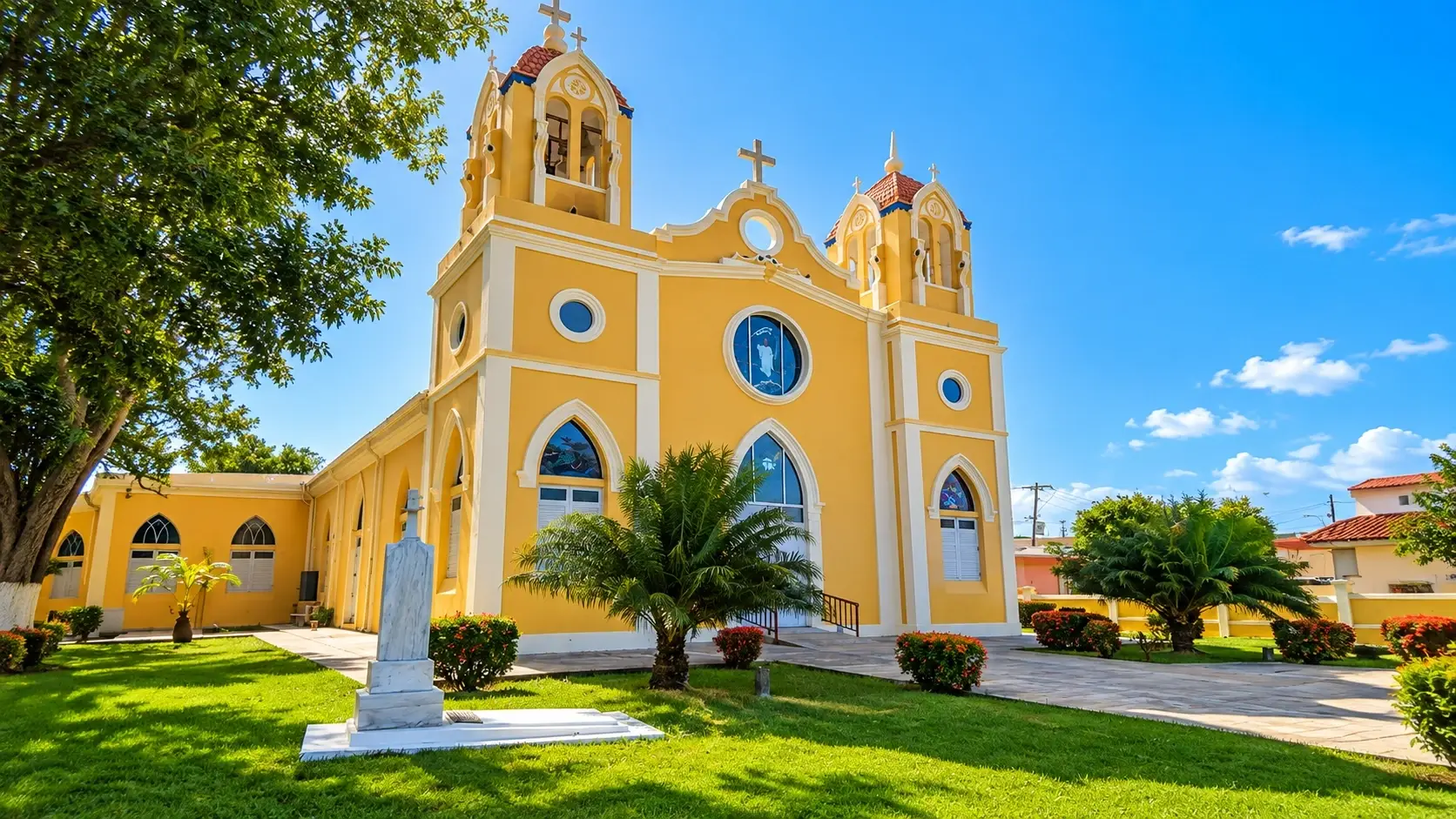 Parroquia San Antonio Abad in Añasco, Puerto Rico, with its yellow historic facade, twin bell towers, landscaped lawn, palms, and blue sky.