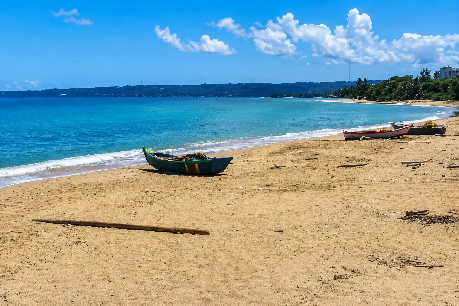 Sandy shoreline in RÃo Grande, Aguada, Puerto Rico, with turquoise ocean water, traditional fishing boats, tropical greenery, distant hills, and a bright Caribbean sky.