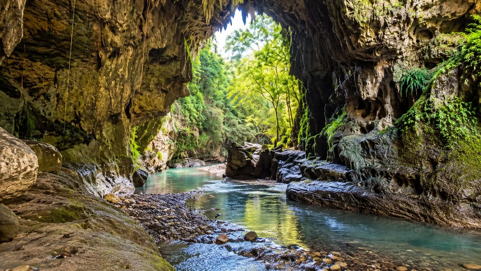 Scenic view representing Río Cagüitas in Aguas Buenas, Puerto Rico, with clear water flowing through a limestone cave surrounded by rocks and lush tropical vegetation.