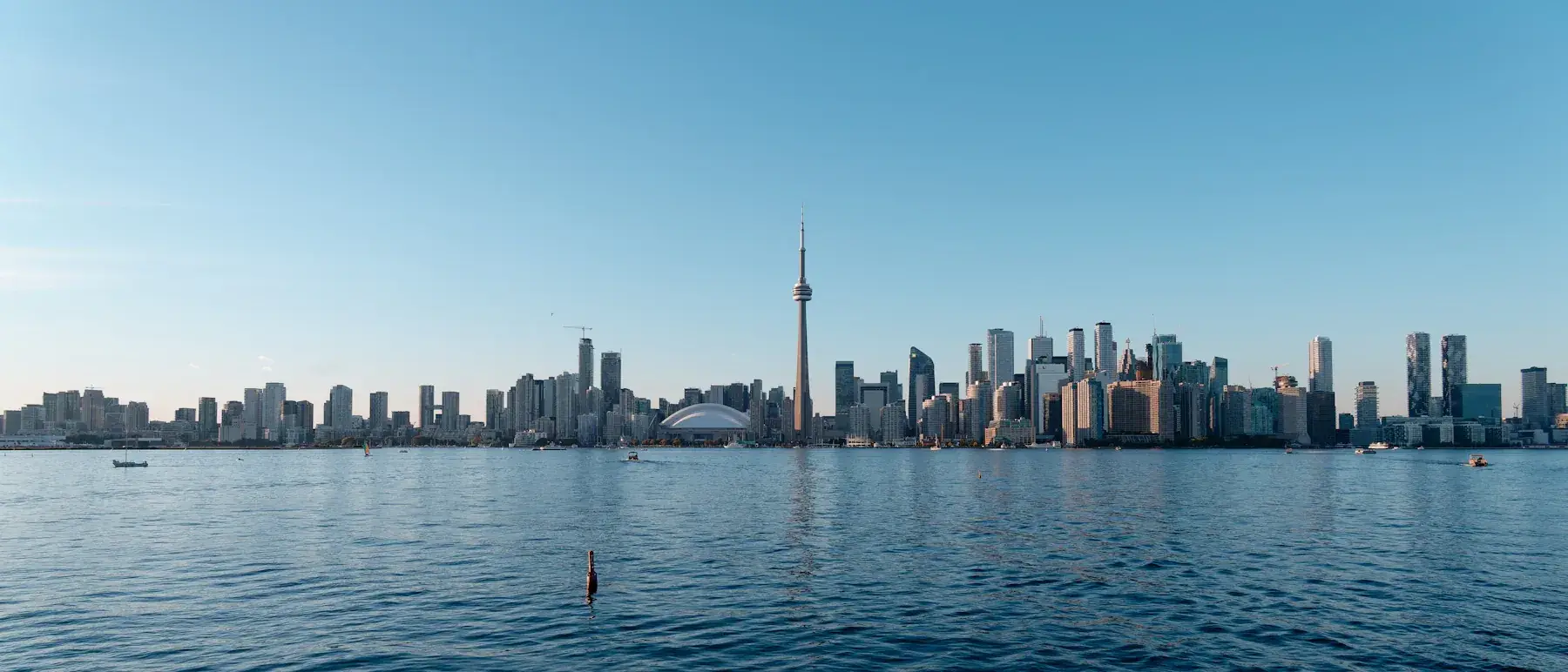CN Tower, downtown high-rise buildings and small boats across Lake Ontario under a clear blue daytime sky in Toronto, Ontario, Canada