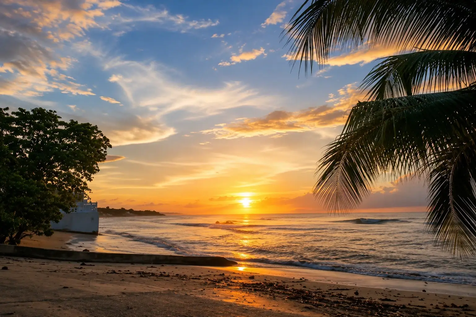 Golden sunset over the ocean in Aguada, Puerto Rico, with gentle waves, a sandy tropical beach, palm trees, and colorful evening clouds.