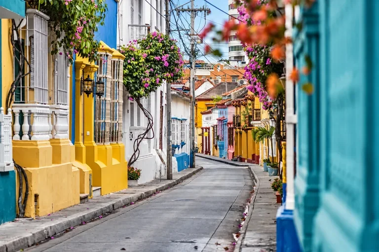 Yellow, white and turquoise colonial façades with flowering balconies along a narrow street in Cartagena, Colombia