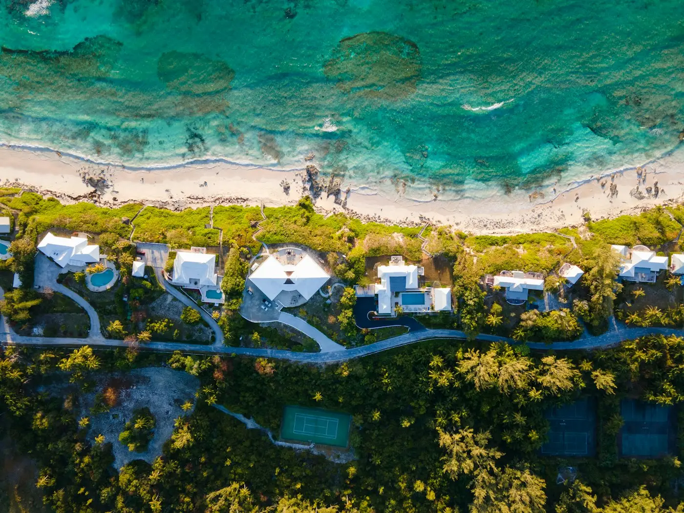 Beachfront homes among tropical trees beside clear water in The Bahamas