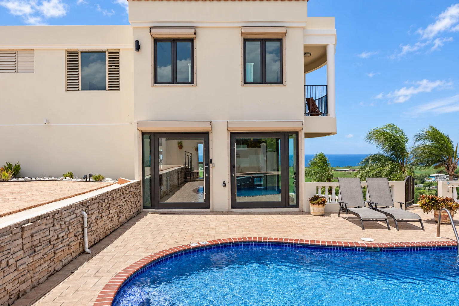 White two-story façade, glass doors, stone terrace and swimming pool at Casa Nakhla in Membrillo, Camuy, Puerto Rico.