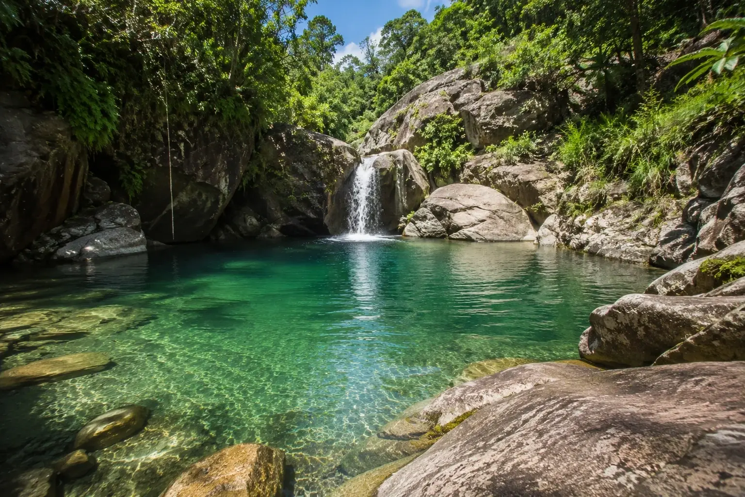 Clear natural swimming pool and waterfall surrounded by tropical vegetation and rocks at Charco El Ataúd in Adjuntas, Puerto Rico.