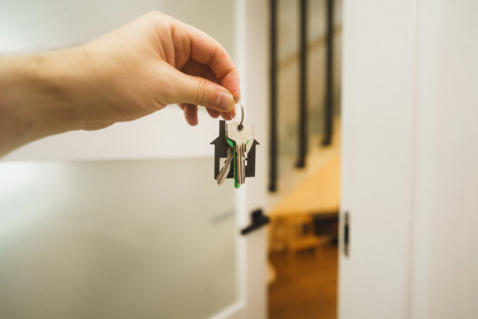 A hand holds a set of house keys beside an open doorway.