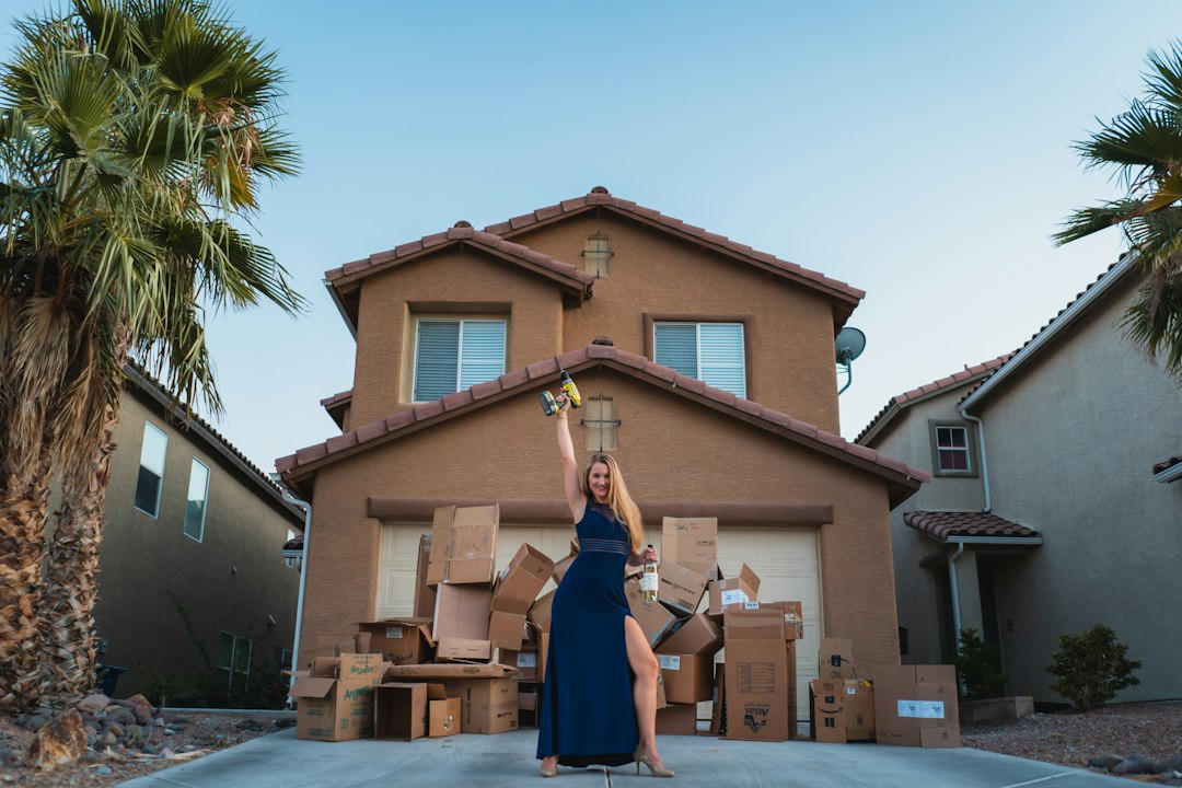 Woman Beside Moving Boxes Outside a House A woman in a blue dress stands beside moving boxes outside a two-story house.