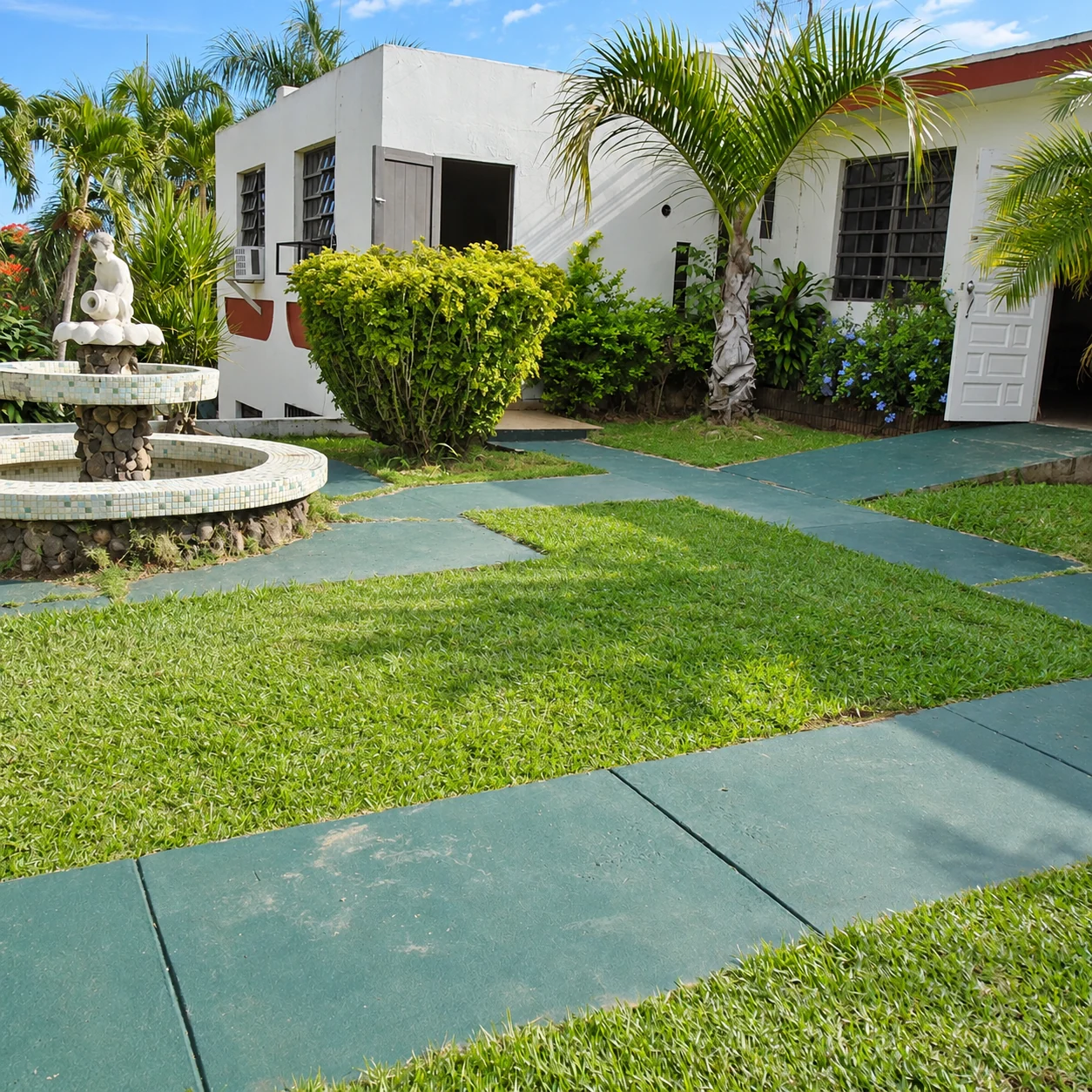 White guesthouse façade, palm trees, shrubs, green paths and a circular fountain in the courtyard at Las Cavernas Guesthouse in Quebrada, Camuy.