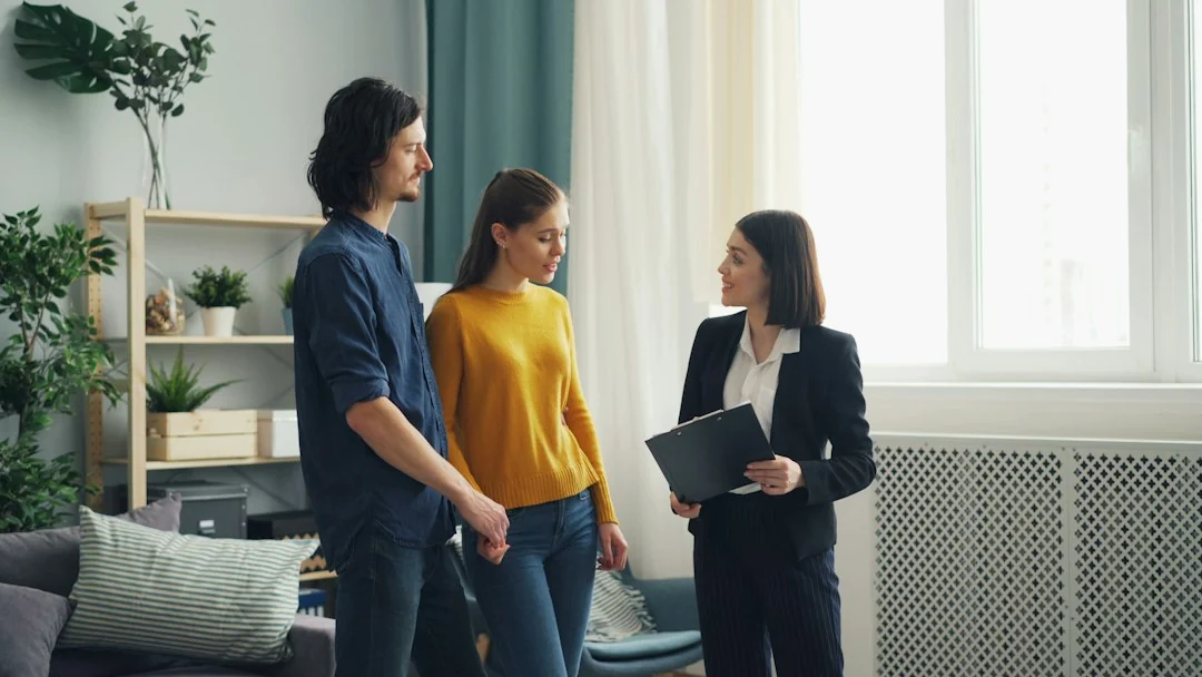 Woman real estate broker speaking with two prospective buyers inside a bright residential living room.