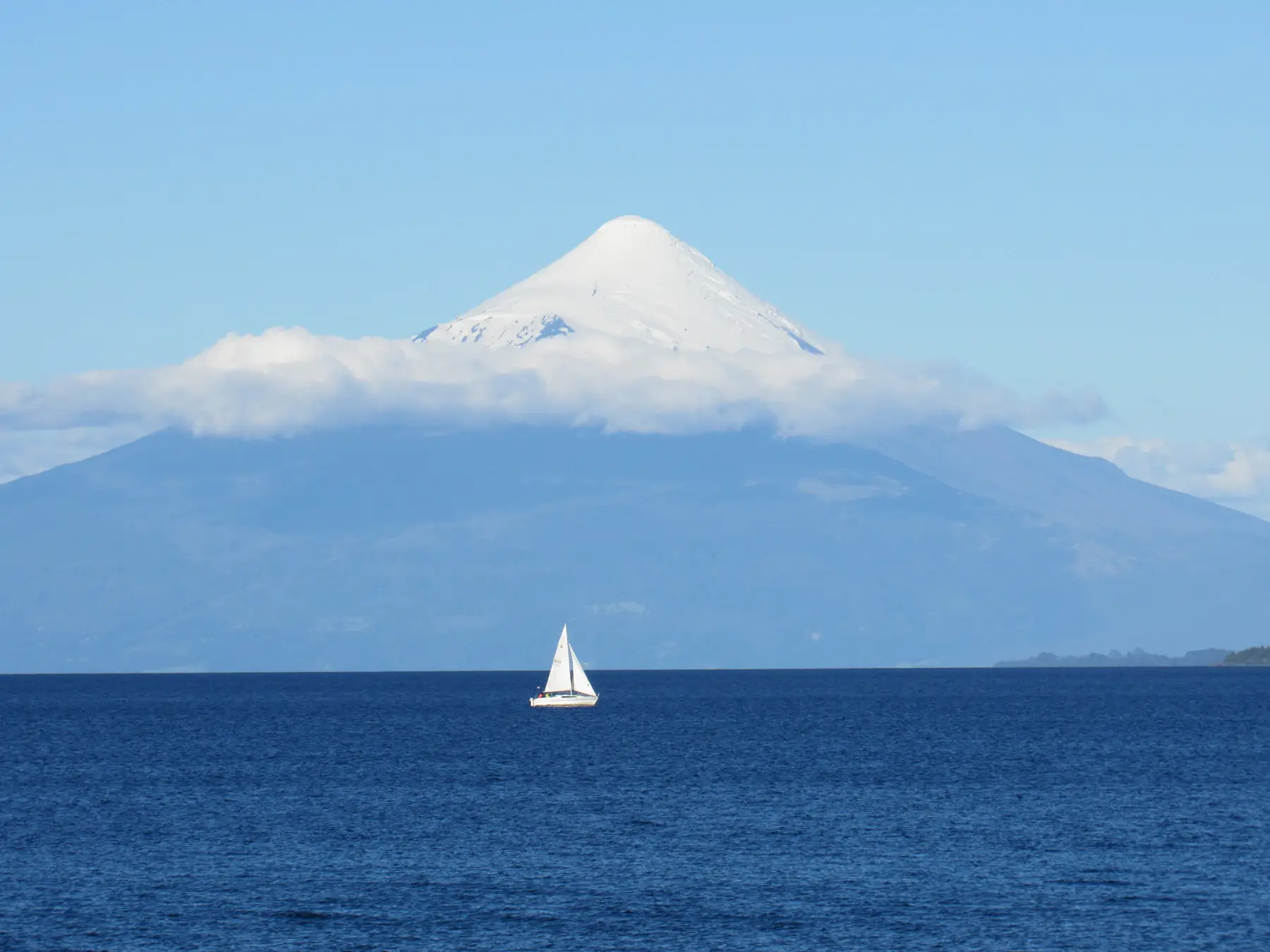 A white sailboat on blue Lake Llanquihue beneath snow-capped Osorno Volcano near Puerto Varas, Chile